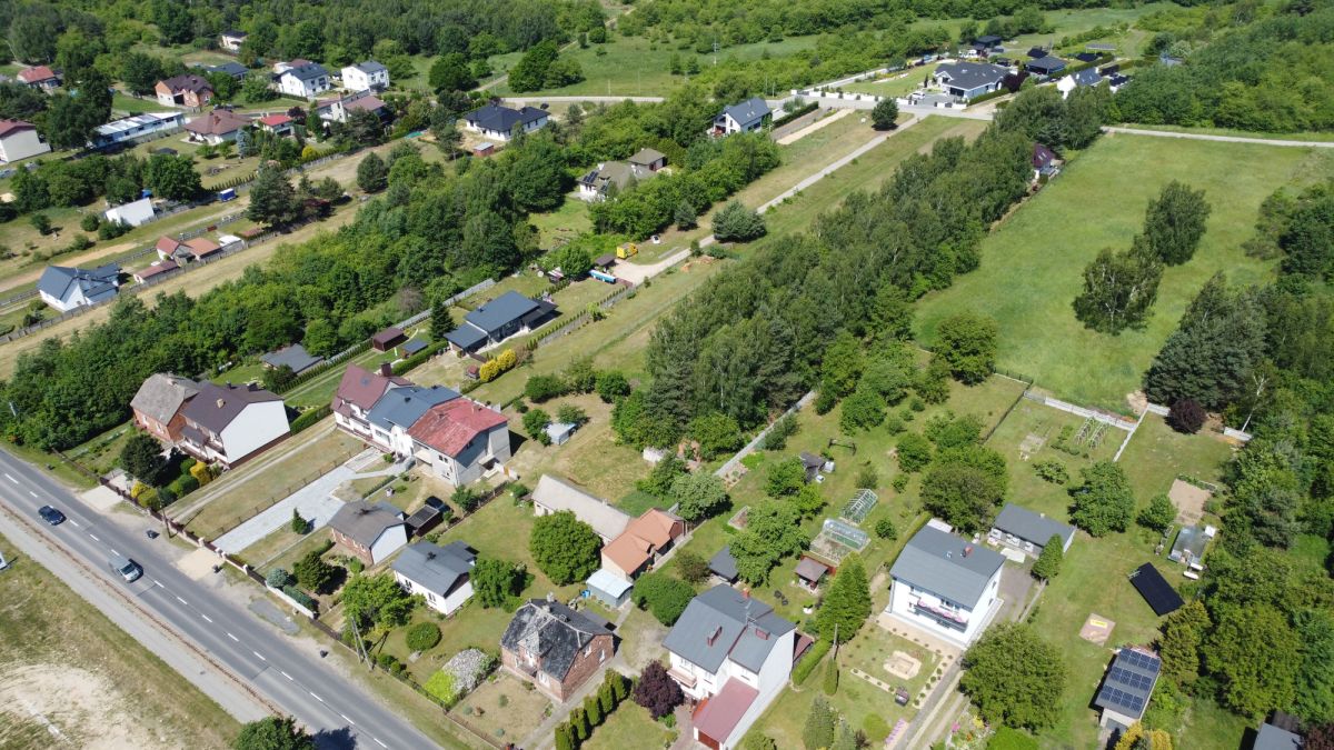 Aerial view of a residential neighborhood with houses, trees, and a large green field bordered by roads and fences.