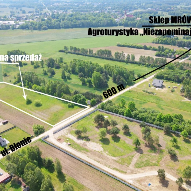 Aerial view of a rural land for sale with outlined plot boundaries and the label 'Działki na sprzedaż' near a road and green fields.