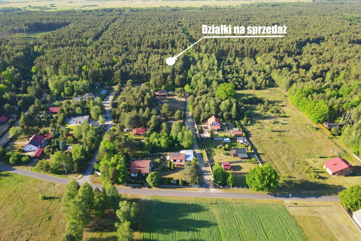 Aerial view of a rural village with houses, roads, and surrounding forest; label 'Działki na sprzedaż' points to plots for sale.
