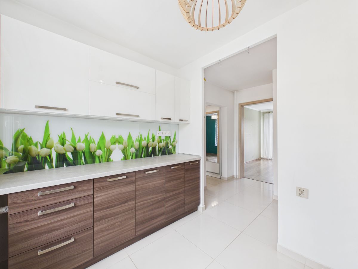 Modern kitchen with white upper cabinets, dark wood lower cabinets, and a tulip backsplash along a light countertop.