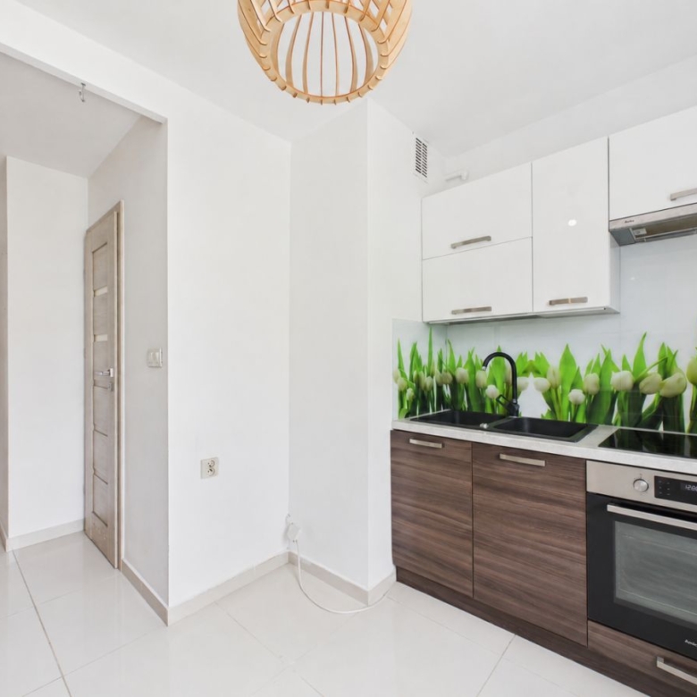Modern kitchen with white upper cabinets, dark wood lower cabinets, and a green tulip backsplash over a black sink and oven area