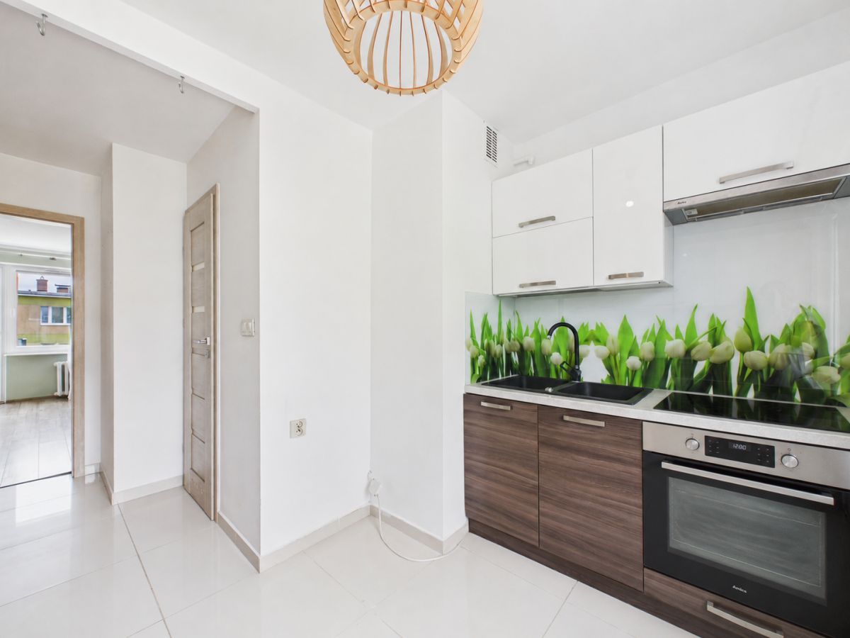 Modern kitchen with white upper cabinets, dark wood lower cabinets, and a green tulip backsplash over a black sink and oven area
