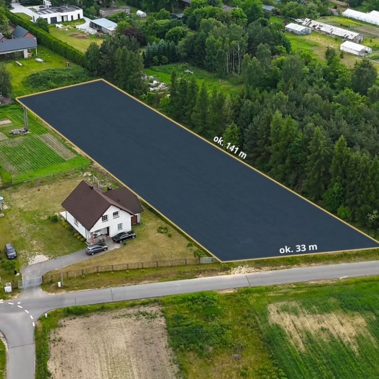 Aerial view of a rectangular plot outlined in yellow beside a white house, dimensions ~141 m by 33 m, in a rural area with fields and trees nearby.