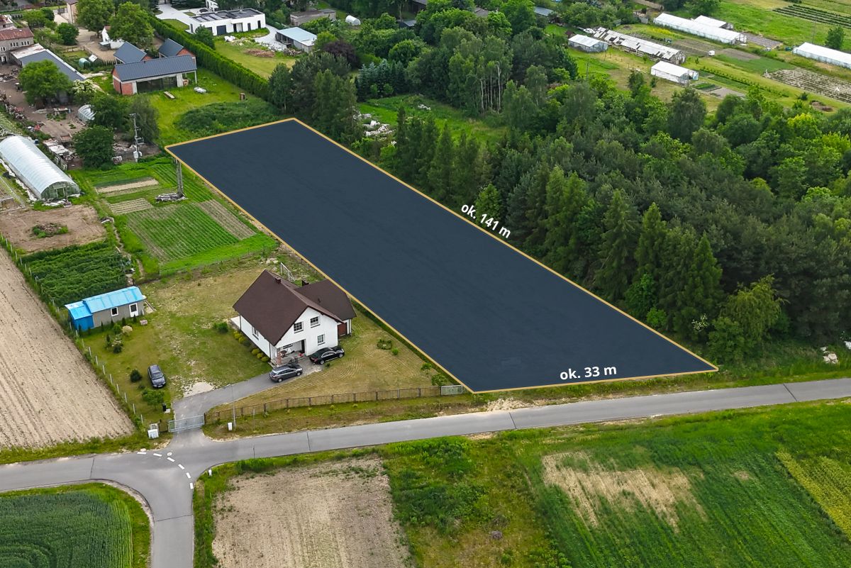 Aerial view of a rectangular plot outlined in yellow beside a white house, dimensions ~141 m by 33 m, in a rural area with fields and trees nearby.