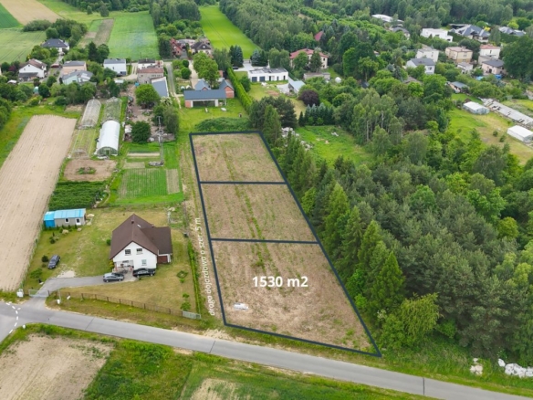 Aerial view of a rural area with a outlined vacant plot of 1,530 m² for sale along a road, surrounded by trees and houses
