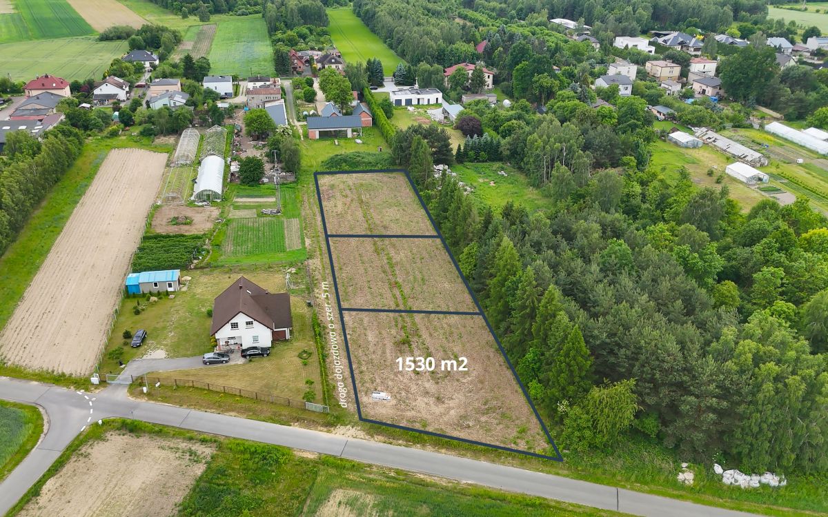 Aerial view of a rural area with a outlined vacant plot of 1,530 m² for sale along a road, surrounded by trees and houses