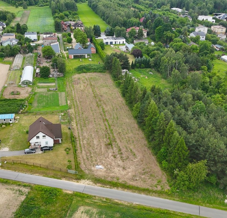 Aerial view of a rural neighborhood with fields, trees, and a road running through the center. suburban houses line the edges of farmland.