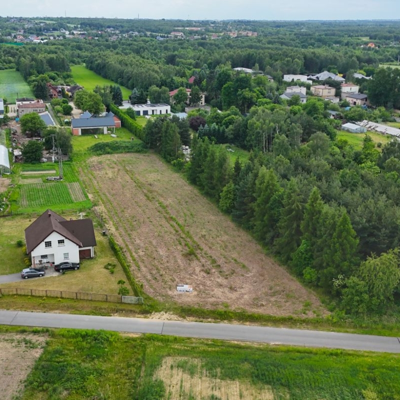 Aerial view of a rural property: white house with cars, surrounding fields, greenhouses, and a road at the foreground.