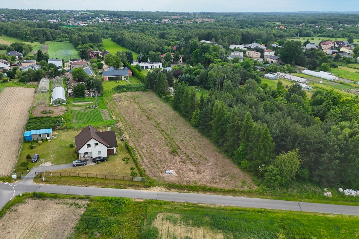 Aerial view of a rural property: white house with cars, surrounding fields, greenhouses, and a road at the foreground.