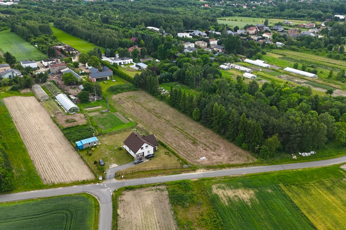 Aerial view of a rural village with fields, greenhouses, and a white house by a road intersection surrounded by trees and farmland