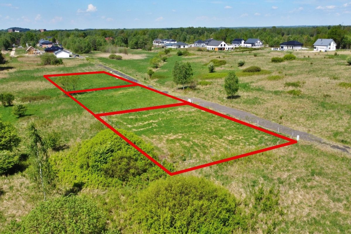 Aerial view of three building plots outlined in red along a road in a developing neighborhood on grassy land near houses in the distance (for sale).
