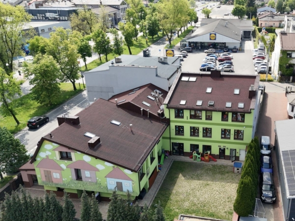Aerial view of a lime-green building with a mural, a small playground, and a Lidl store in the distance among trees and streets.
