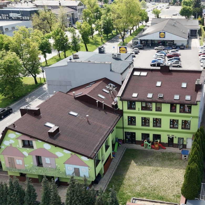Aerial view of a lime-green building with a mural, a small playground, and a Lidl store in the distance among trees and streets.