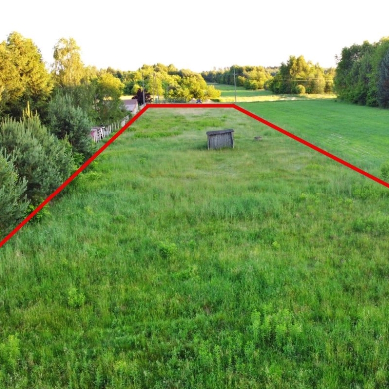 Aerial view of a green field with red boundary lines marking a triangular plot, small shed near center, trees along left and right edges.