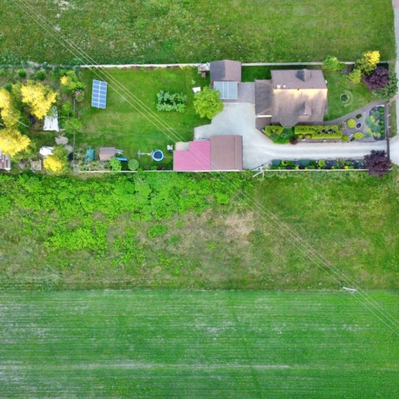 Aerial view of a rural property with a house, yard, solar panels, and surrounding fields, top-down perspective.