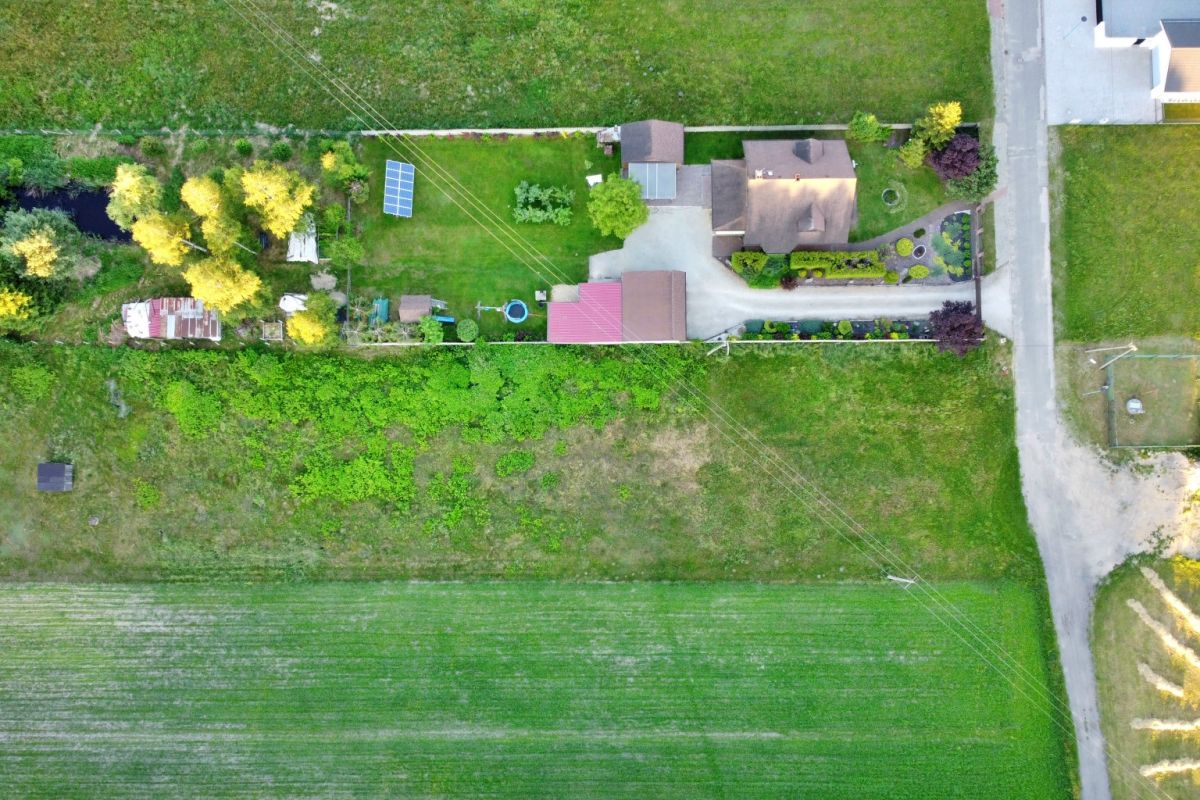 Aerial view of a rural property with a house, yard, solar panels, and surrounding fields, top-down perspective.