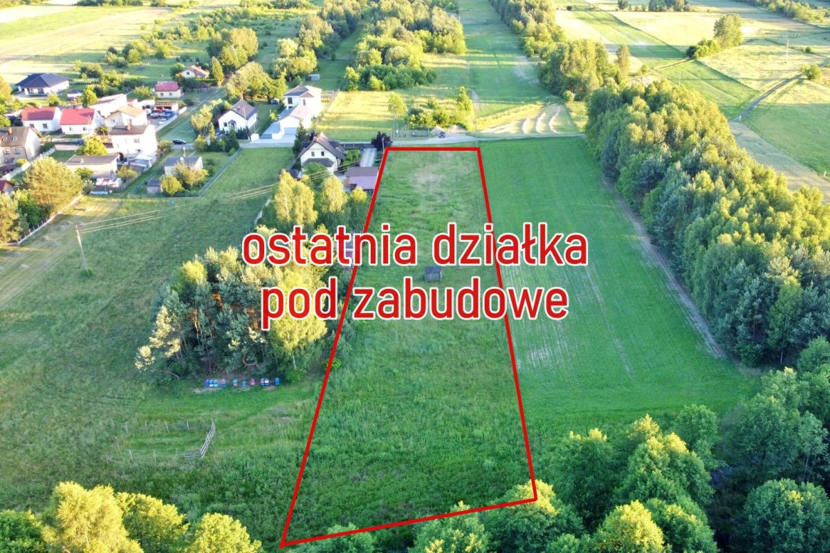 Aerial view of a triangular plot outlined in red in a green field, with nearby houses and the Polish text 'ostatnia działka pod zabudowę' overlays