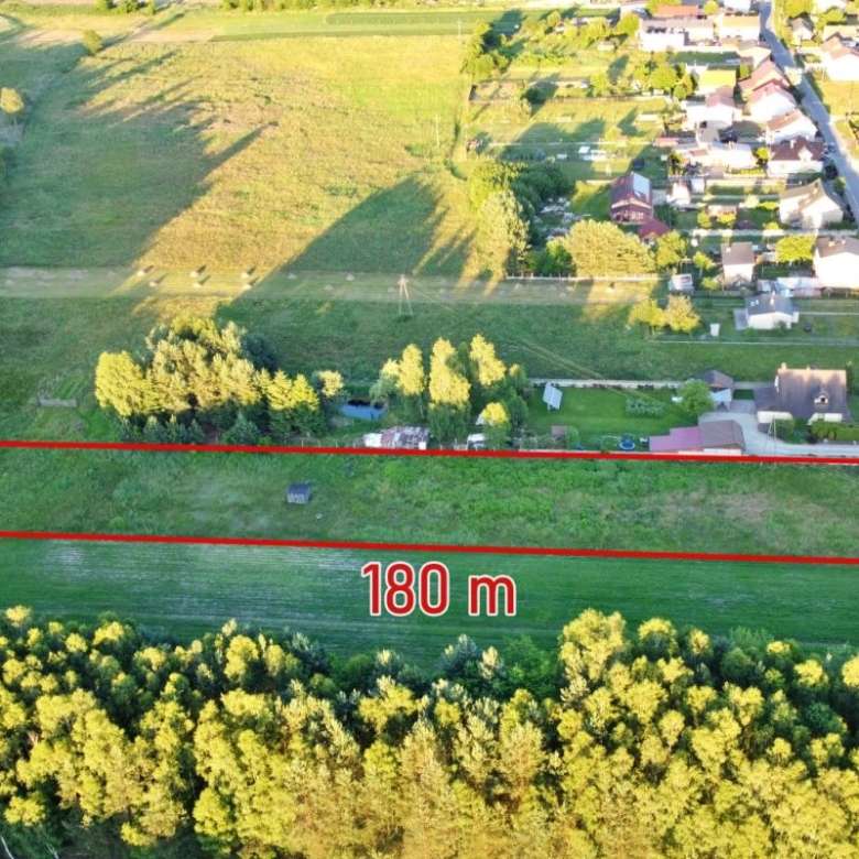 Aerial view of a rectangular grassy plot outlined in red, 180 m long, bordered by a road and surrounding fields near a village.