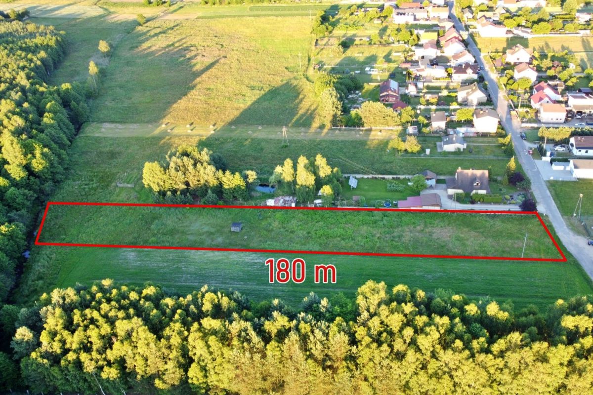 Aerial view of a rectangular grassy plot outlined in red, 180 m long, bordered by a road and surrounding fields near a village.