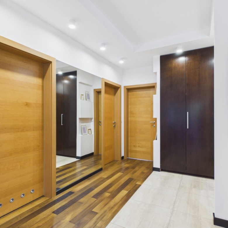Modern hallway with light wood doors, a tall dark wardrobe, and a mirrored wall reflecting more doors and storage ideas inside a contemporary home.