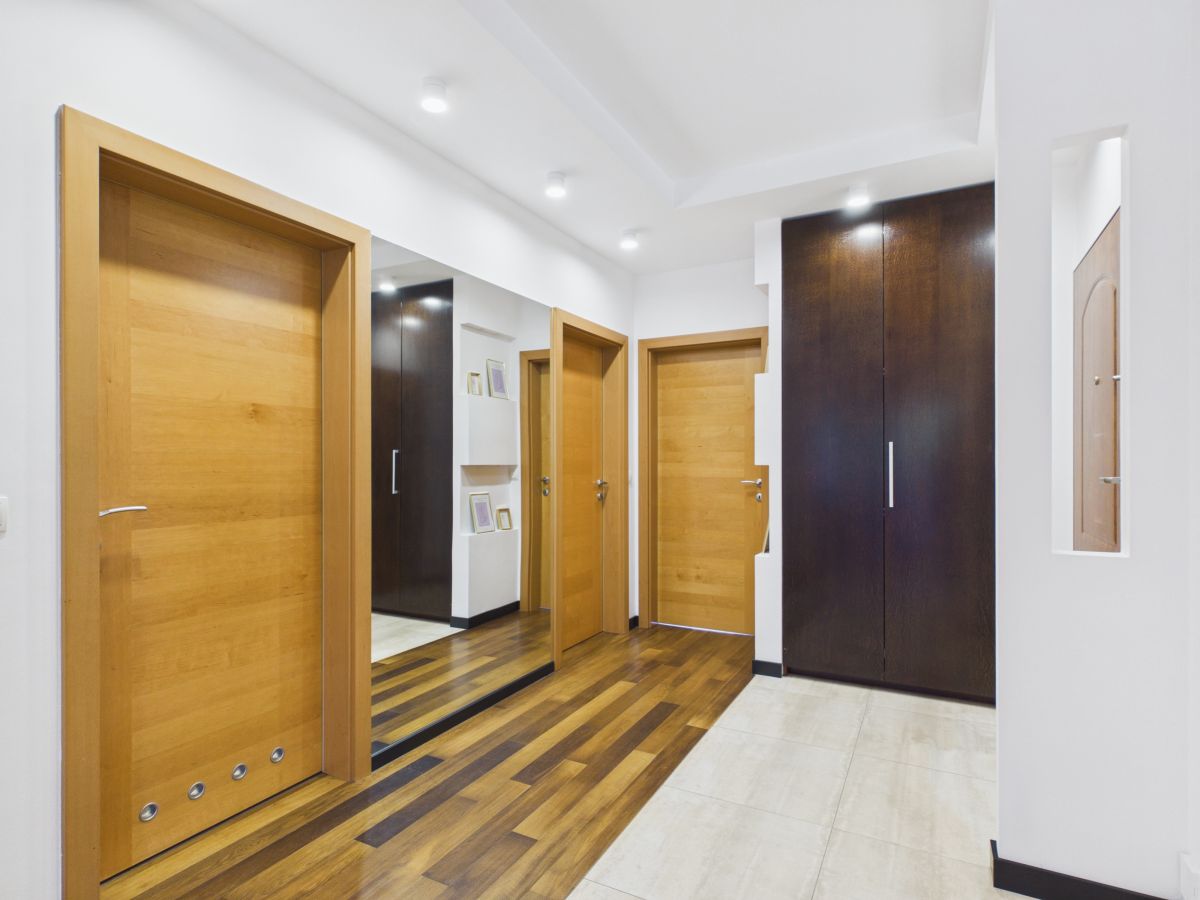 Modern hallway with light wood doors, a tall dark wardrobe, and a mirrored wall reflecting more doors and storage ideas inside a contemporary home.