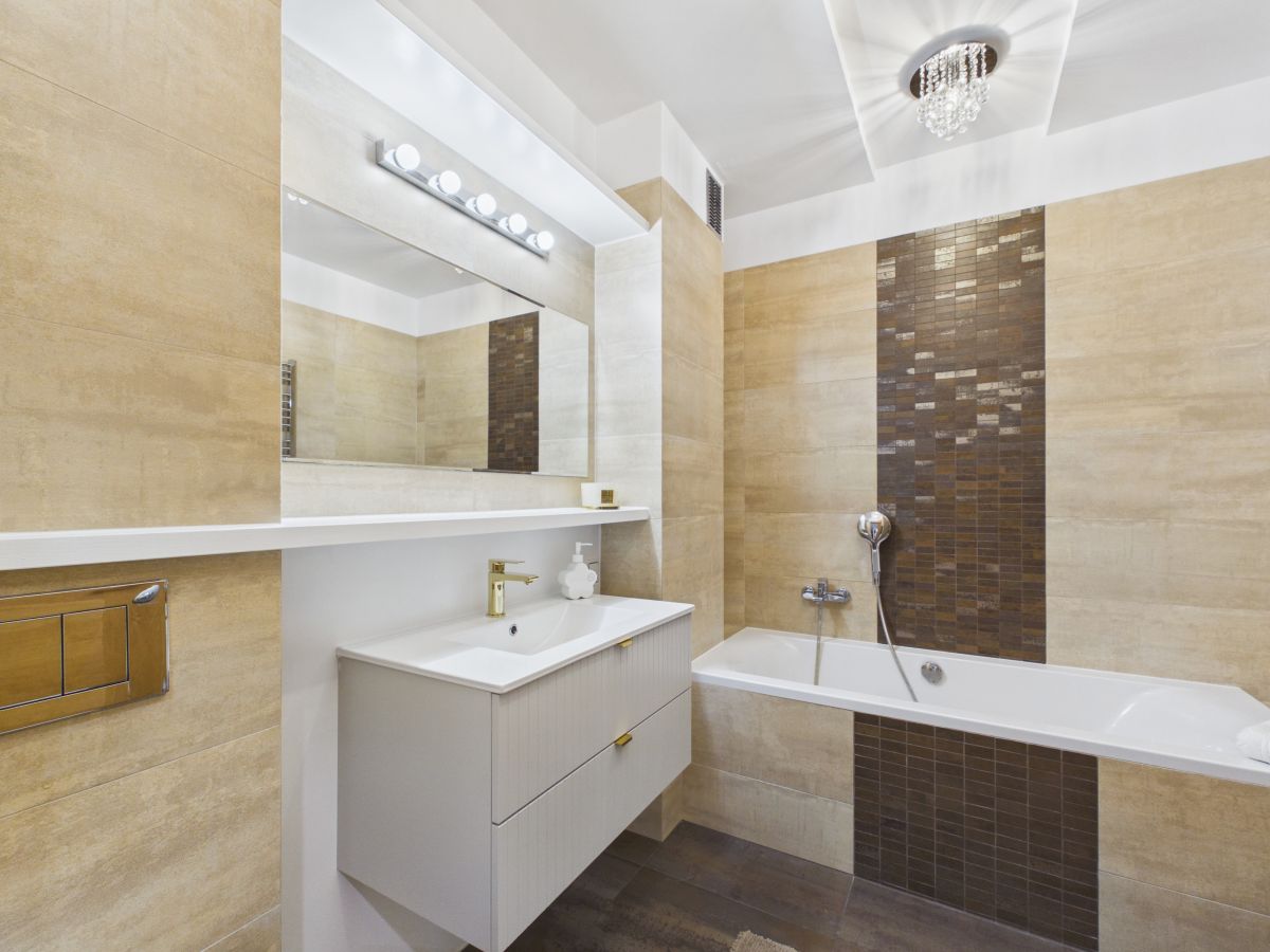 Modern bathroom with a white vanity, sink, and large mirror beneath a row of lights.