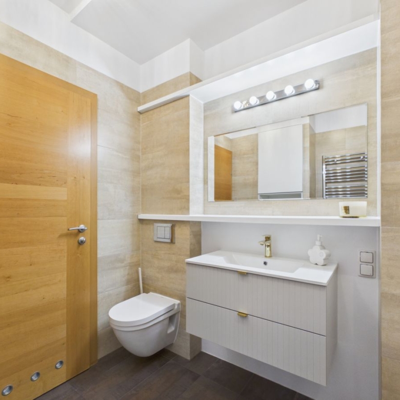 Modern bathroom with wall-mounted toilet, white vanity, large mirror, and beige tile walls in a bright space.