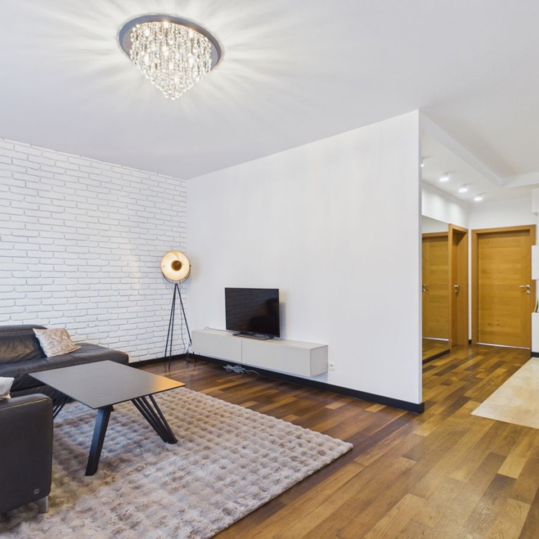 Modern living room with white brick accent wall, chandelier, dark leather sofa, and a rectangular coffee table on a light rug.