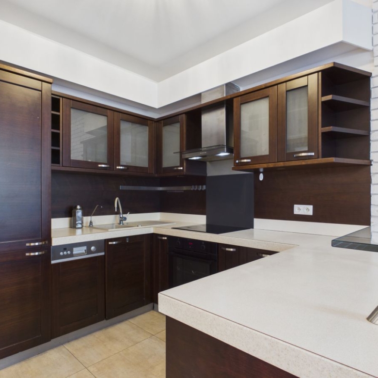 U-shaped kitchen with dark wood cabinets, white countertops, and stainless steel appliances.