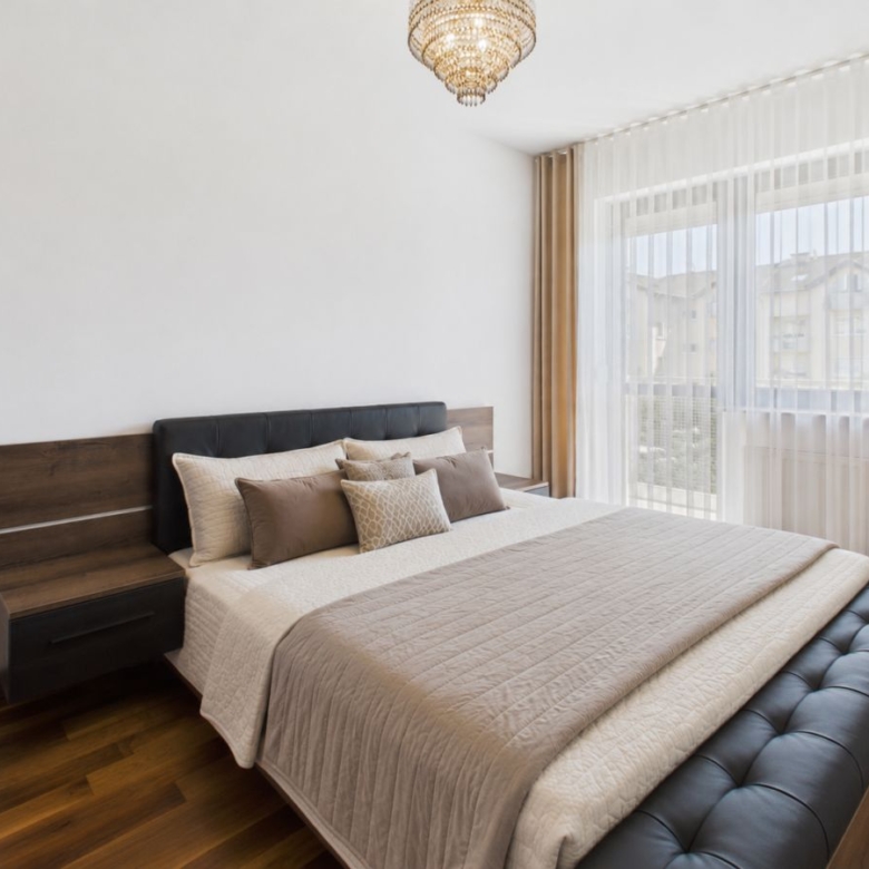 Modern bedroom with a large bed, tufted black bench at the foot, and two nightstands under warm lighting.