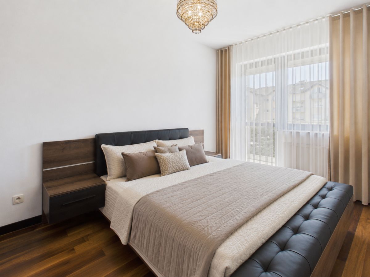 Modern bedroom with a large bed, tufted black bench at the foot, and two nightstands under warm lighting.