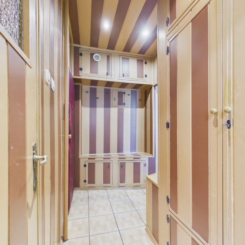 Narrow hallway with built-in beige cabinets and purple-brown striped walls, tiled floor, and overhead storage.