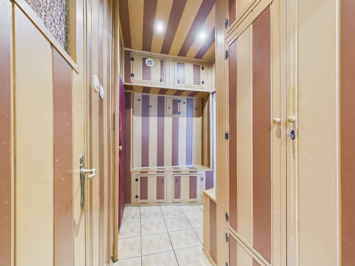 Narrow hallway with built-in beige cabinets and purple-brown striped walls, tiled floor, and overhead storage.