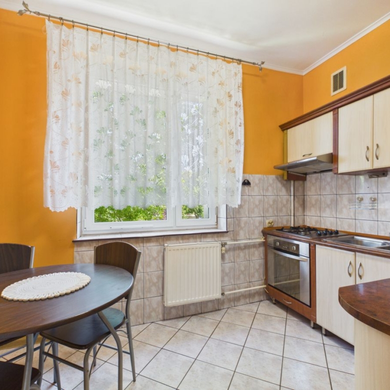 Cozy kitchen with orange walls, a lace-curtained window, and a round dining table with chairs in the foreground.