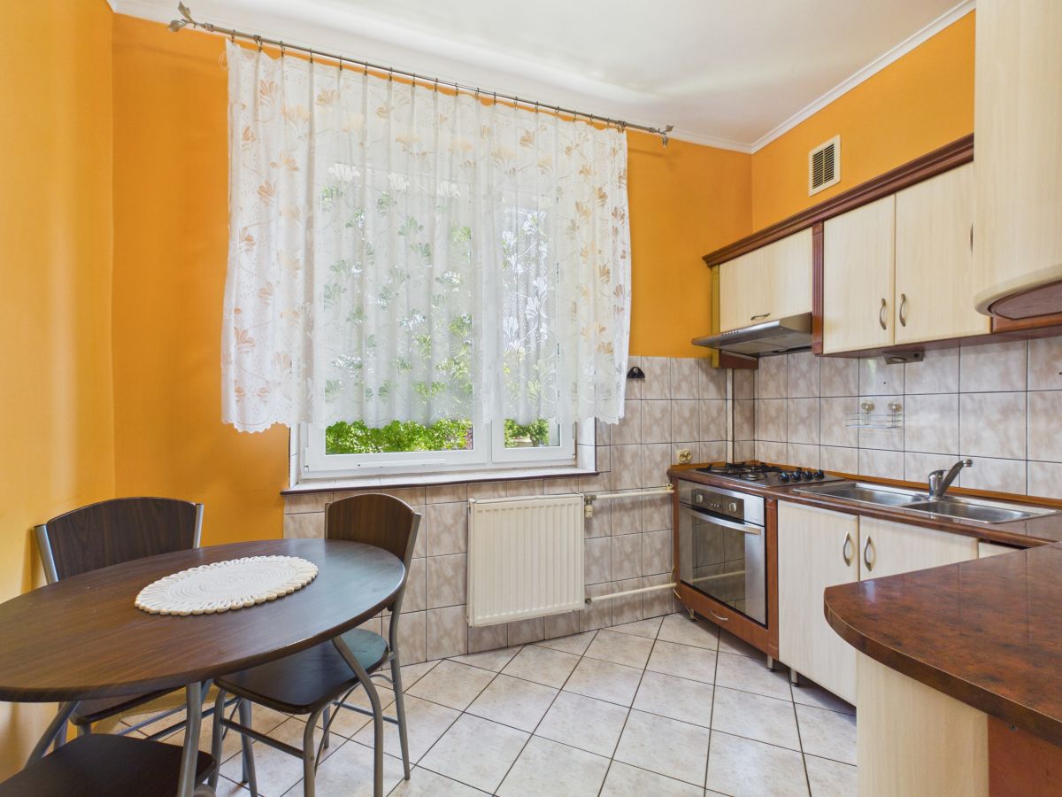 Cozy kitchen with orange walls, a lace-curtained window, and a round dining table with chairs in the foreground.