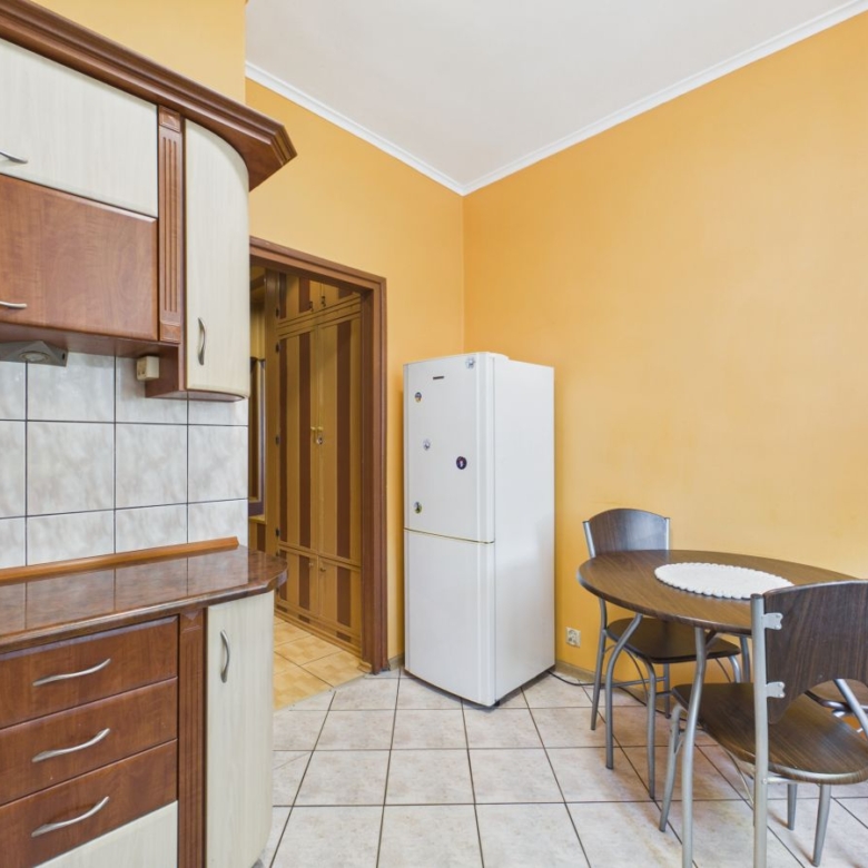 Kitchen with orange walls, wooden cabinets, tiled backsplash, a white refrigerator, and a round dining table with four chairs nearby.
