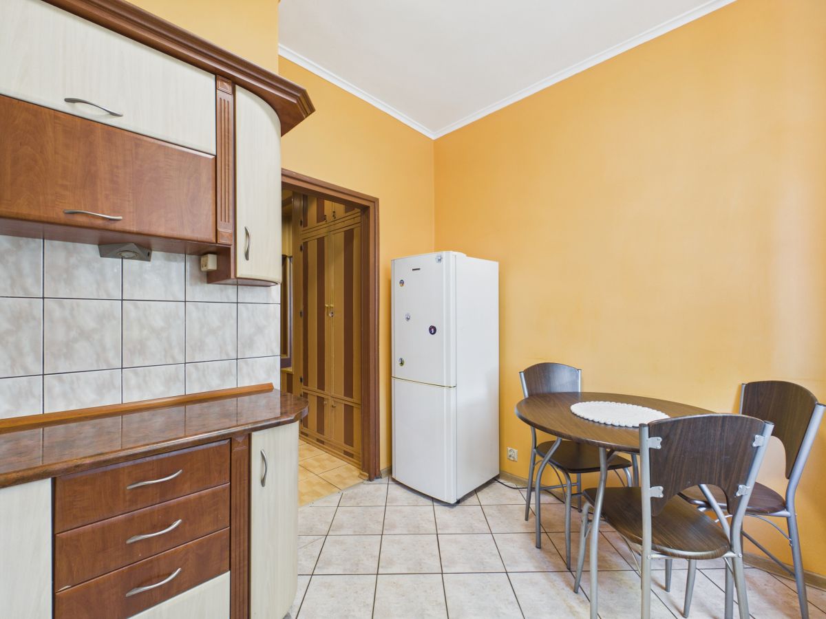 Kitchen with orange walls, wooden cabinets, tiled backsplash, a white refrigerator, and a round dining table with four chairs nearby.