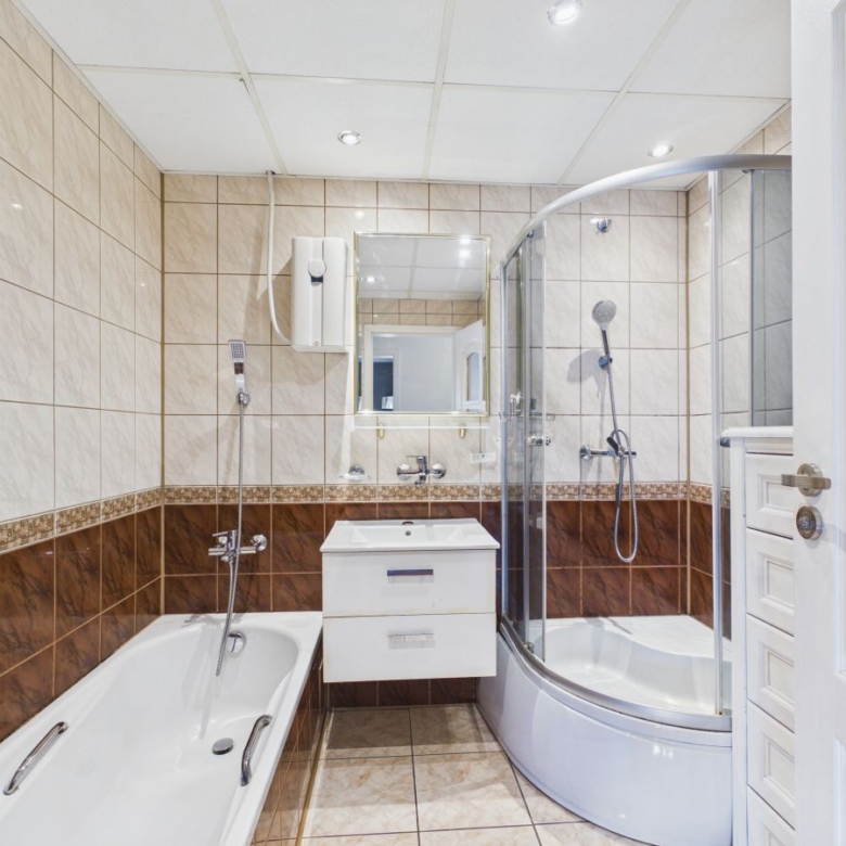 Modern bathroom with curved glass shower, white vanity with two drawers, and a bathtub along tiled walls.