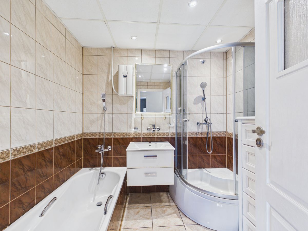 Modern bathroom with curved glass shower, white vanity with two drawers, and a bathtub along tiled walls.