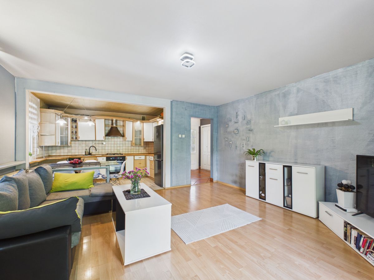 Open-plan living room and kitchen with light wood floors, gray sofa, white coffee table, and blue textured walls of the main area.