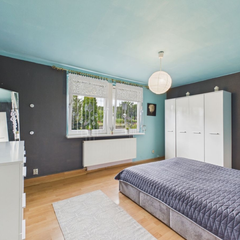Bedroom with teal ceiling and dark gray walls, white furniture, and a low gray bedspread; window with lace curtains and a white wardrobe opposite the bed.
