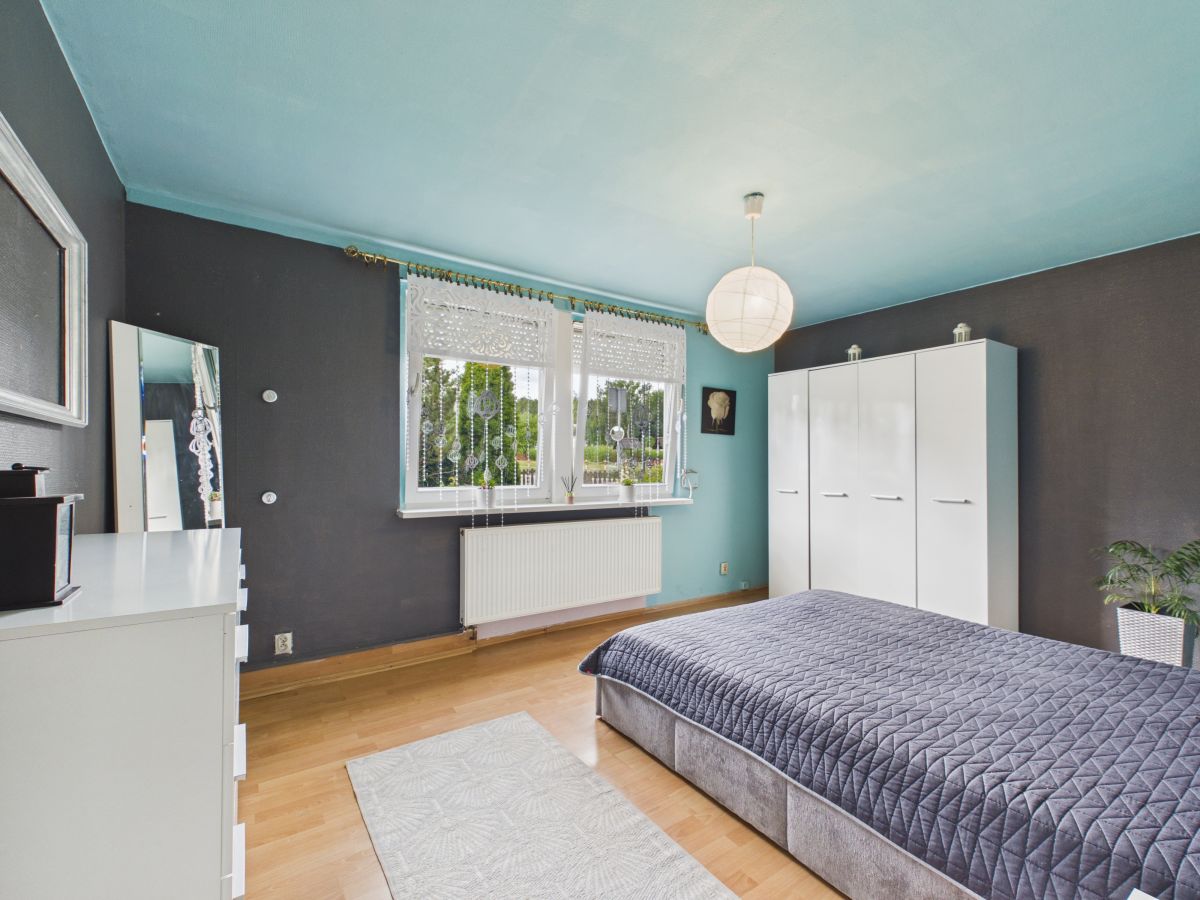 Bedroom with teal ceiling and dark gray walls, white furniture, and a low gray bedspread; window with lace curtains and a white wardrobe opposite the bed.