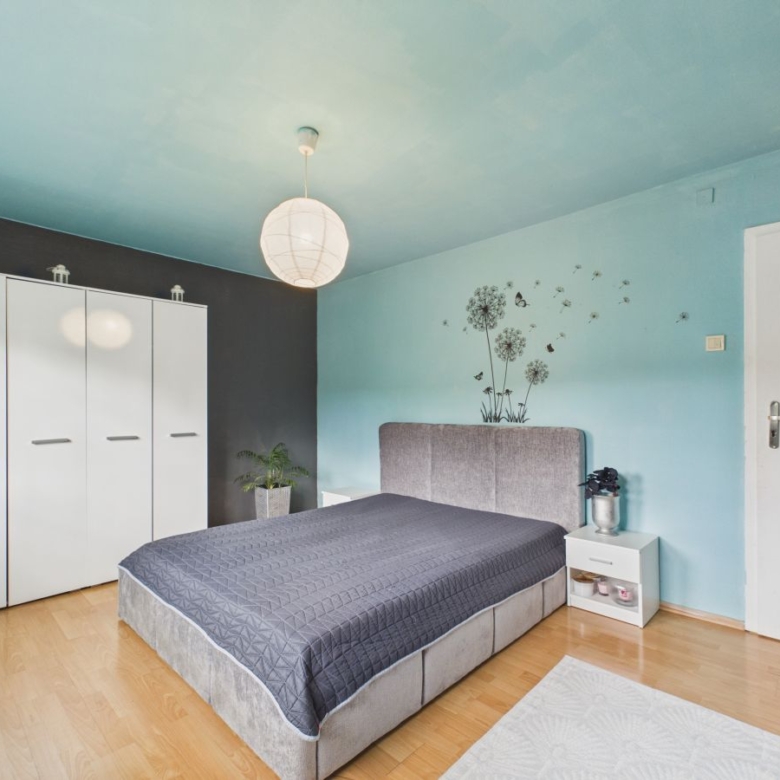 Bright bedroom with a light wood floor, blue walls, and a large white wardrobe against a dark accent wall