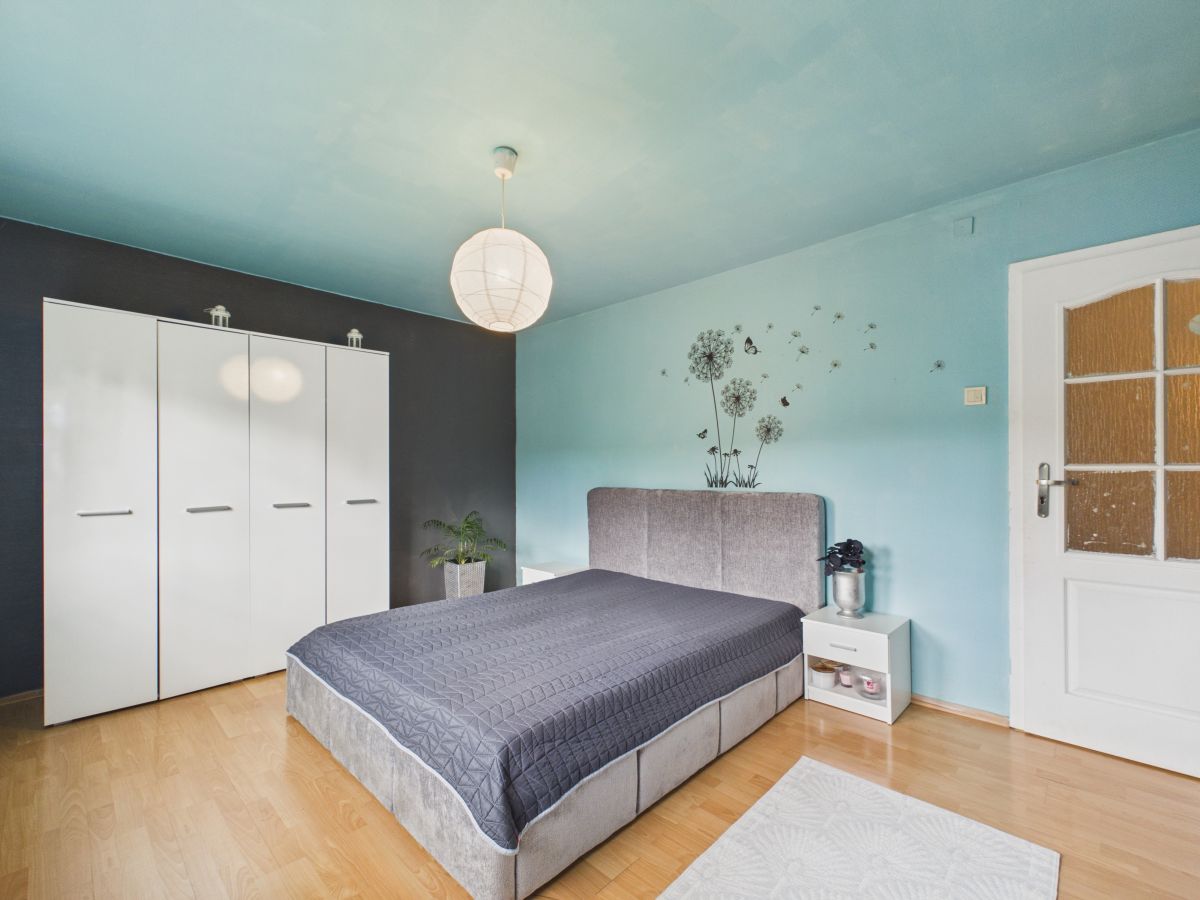 Bright bedroom with a light wood floor, blue walls, and a large white wardrobe against a dark accent wall