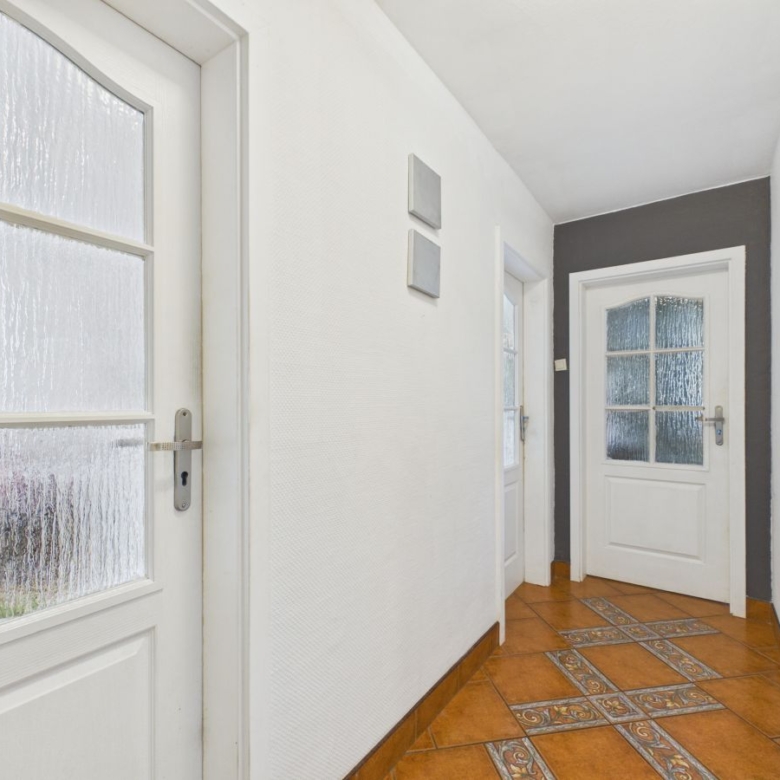 White hallway with frosted glass-panel doors and a decorative tiled floor pattern in brown tones.
