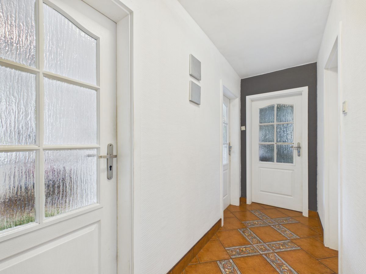 White hallway with frosted glass-panel doors and a decorative tiled floor pattern in brown tones.