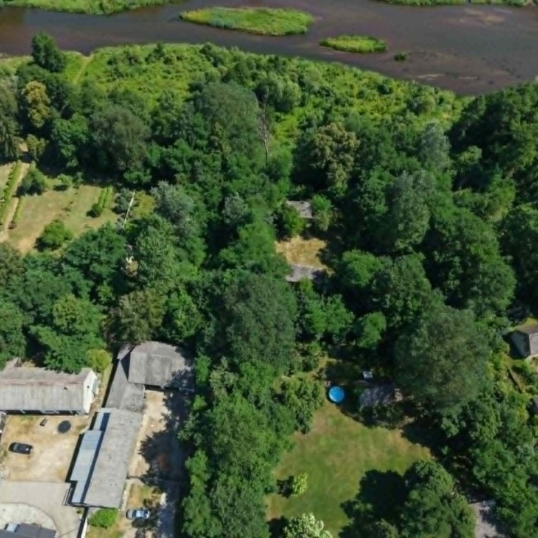 Aerial view of a wooded residential area with houses along the bottom and a blue circular pool in a grassy yard, with a river in the background.