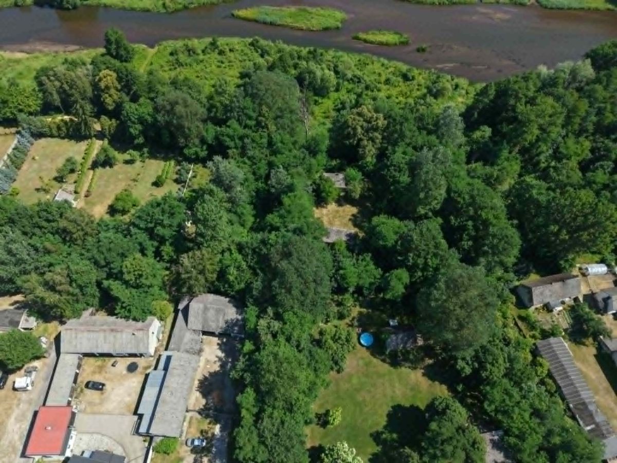 Aerial view of a wooded residential area with houses along the bottom and a blue circular pool in a grassy yard, with a river in the background.