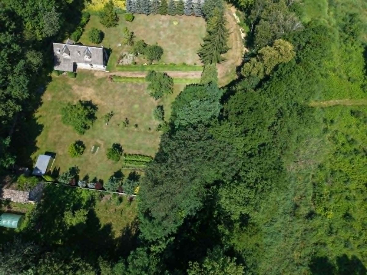 Aerial view of a rectangular garden with a small house on the left and dense trees surrounding the yard.