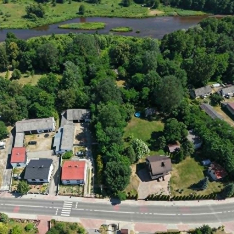 Aerial view of a small neighborhood along a curved road, with red- and gray-roofed houses and dense trees, and a river in the background.